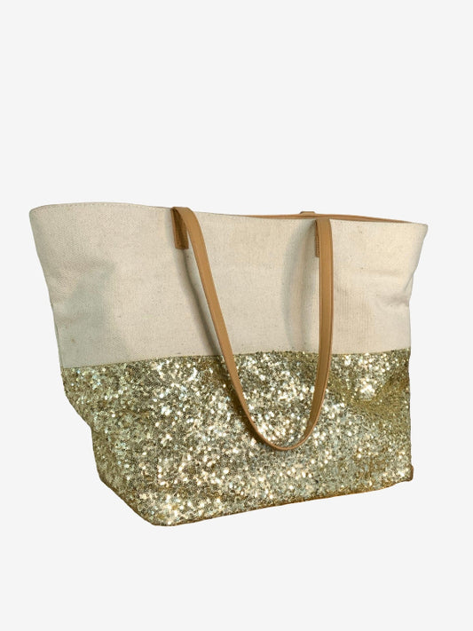 A tote bag with a natural canvas upper half, a gold sequined lower half, and tan shoulder straps, shown against a plain light gray background.