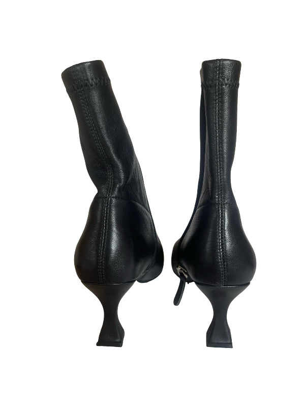 A pair of black leather ankle boots with a unique sculptural flared heel, shown from the back on a plain white background.