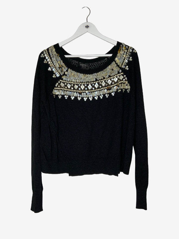 A black long-sleeve knit sweater with intricate silver and white beaded geometric embroidery across the chest, hanging on a white hanger against a light gray background.