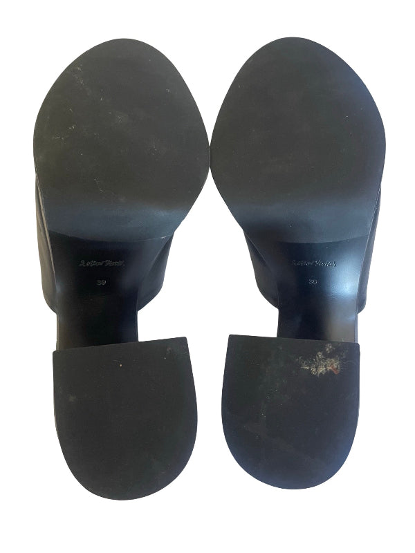 A pair of black block heel sandals shown from the sole view, displaying the outsoles and heel bases against a plain white background.