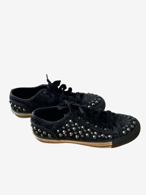 A pair of black low-top lace-up sneakers decorated with silver metallic studs, shown against a plain light gray background.