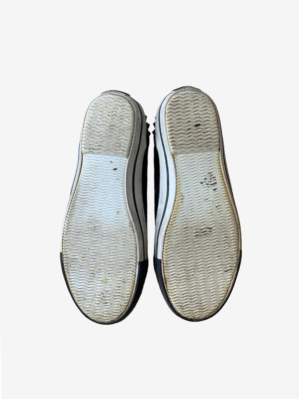 The soles of a pair of black and white low-top sneakers, showing a little dirt and light wear on the textured rubber tread, photographed from a top-down view against a light gray background.