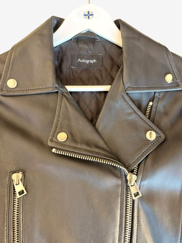 A black leather motorcycle jacket with gold-tone metal snaps and zippers, hanging on a white hanger with the brand name 'Autograph' visible on the inner label.