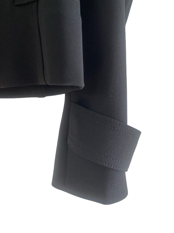 Close-up detail of a black tailored jacket sleeve with a folded cuff and visible stitching, shown against a plain white background.