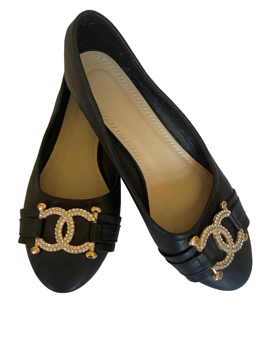 A pair of black faux leather  style ballet flats featuring the signature interlocking CC logo embellished with rhinestones on the front straps, shown against a plain white background.