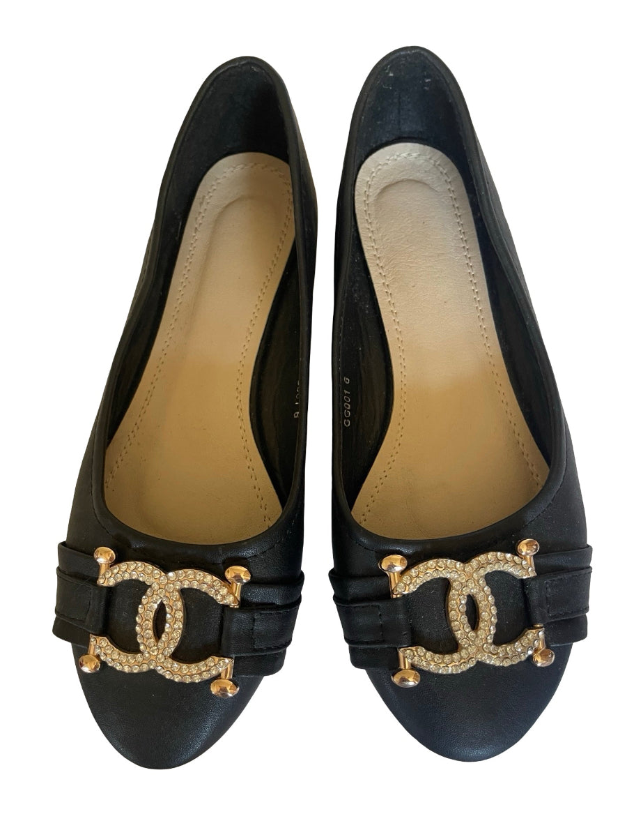 A pair of black leather Chanel style flats featuring the signature interlocking CC logo embellished with rhinestones in gold-tone metal at the vamp.