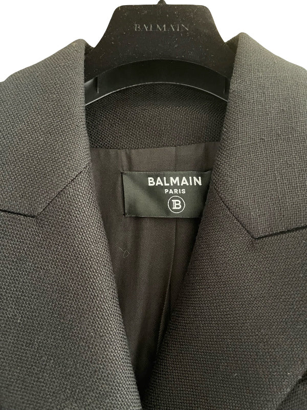 Close-up of a Balmain black textured wool blazer jacket hanging on a black hanger, showing the interior neck label with the Balmain Paris logo.