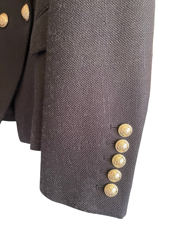 Close-up of a black textured blazer sleeve featuring five decorative gold buttons along the cuff.