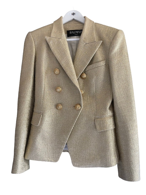 A Balmain double-breasted blazer in textured champagne gold beige textured weave, featuring gold buttons and a white hanger, shown against a plain white background.