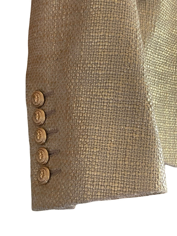 Close-up of a textured blazer sleeve in a metallic gold fabric, featuring five decorative gold buttons on the cuff, set against a plain white background.