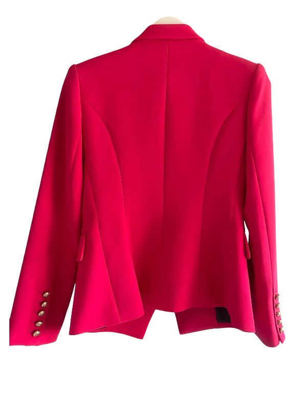 A bright pinkish-red structured blazer shown from the back, featuring a high collar, curved seam details, and decorative metallic buttons on the sleeve cuffs, displayed on a hanger against a white background.