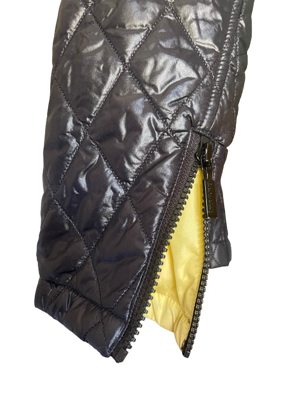 Close-up of a black quilted puffer jacket with a diagonal split zipper opening to reveal a bright yellow interior lining, set against a plain white background.