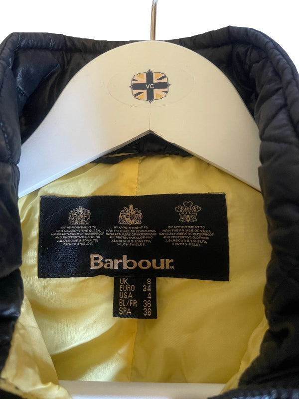 Close-up of a black puffer jacket with a yellow interior lining, hanging on a white hanger. The inner neck label clearly shows the brand 'Barbour'.