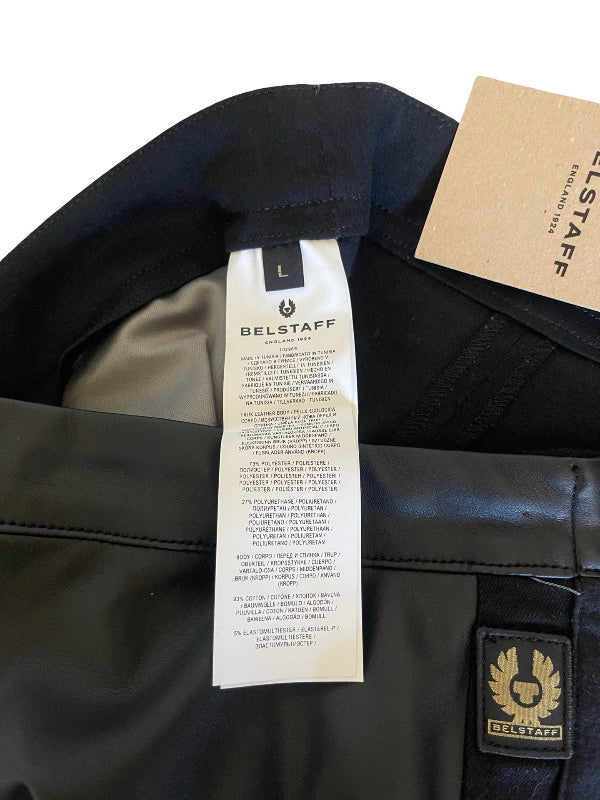 Close-up of a Belstaff jacket interior showing the black fabric lining, a white size tag, a kraft paper hangtag, and a small gold-and-black Belstaff logo patch.