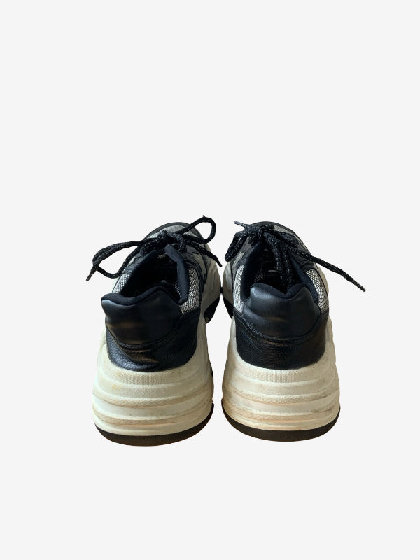 A pair of low-top sneakers shown from the back, featuring black leather uppers with silver metallic side stripes and chunky cream-colored stacked platform soles.