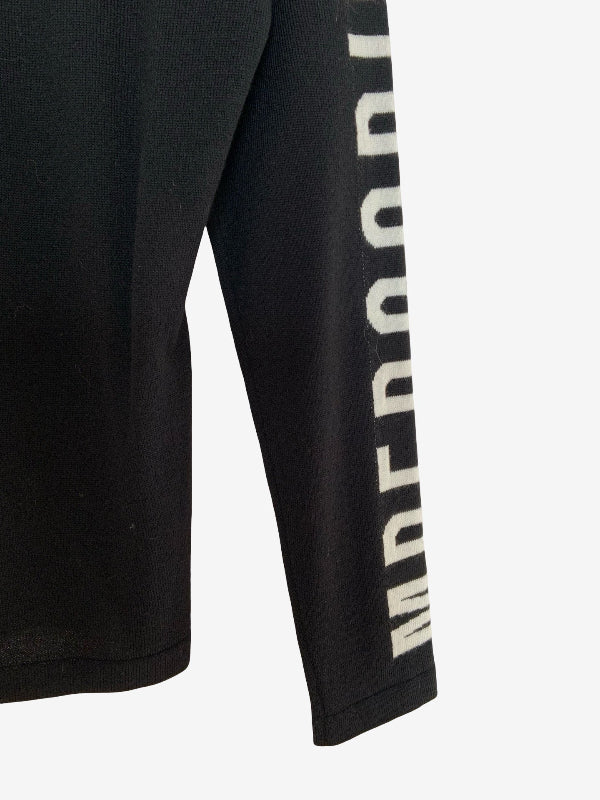 Close-up of a black long-sleeve garment with large vertical white text printed down one sleeve, shown against a light gray background.