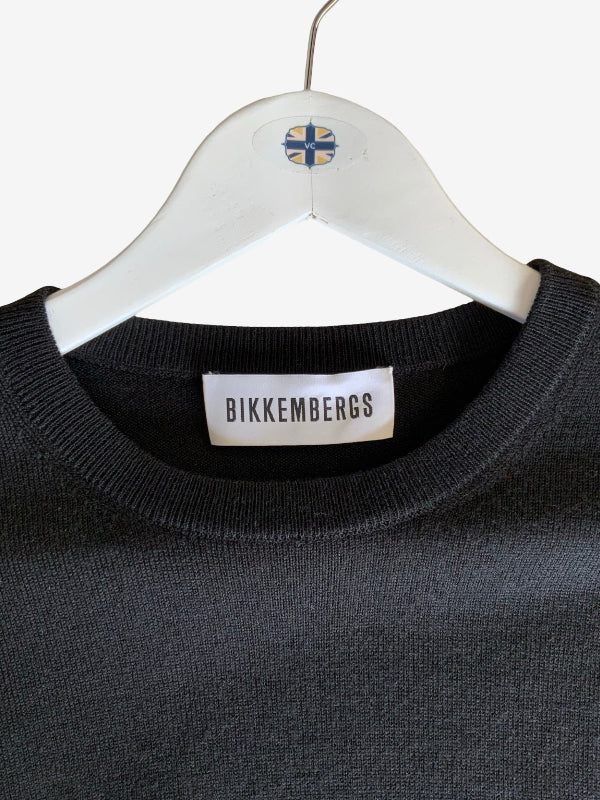 A close-up of a black  knit crewneck sweater hanging on a white wooden hanger. The brand label 'BIKKEMBERGS” is clearly visible on the inside collar, and the hanger features a small Venus Cow Union Jack flag emblem.