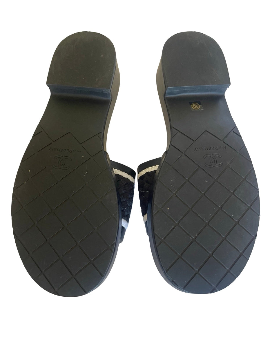 The soles of a pair of dark navy blue quilted slide sandals, showing the textured black rubber outsoles with a small gold logo stamp.