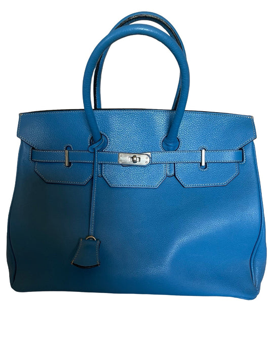 A blue leather handbag with double top handles, a front flap, silver-tone hardware, and a hanging clochette, photographed against a plain white background.