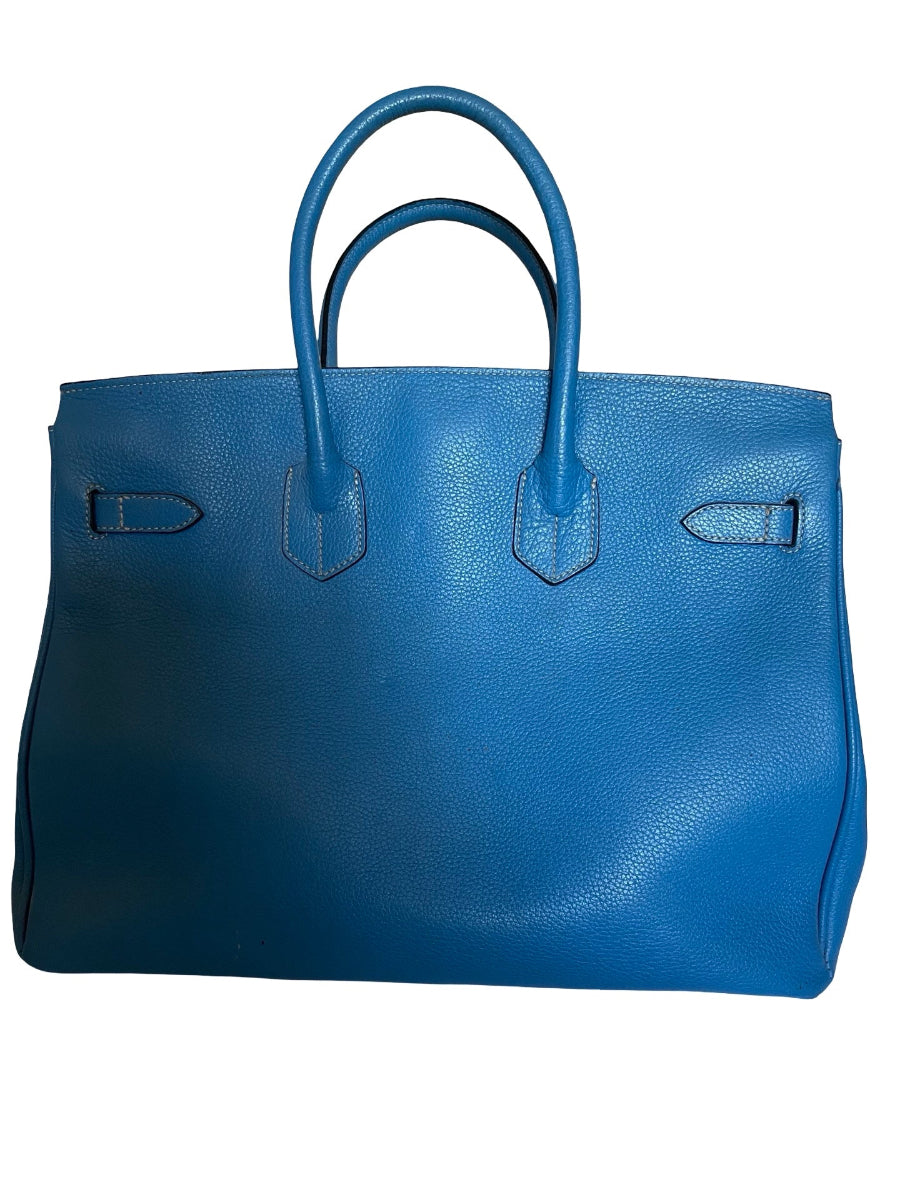 A blue pebbled leather handbag with double top handles and silver-tone hardware, photographed against a plain white background.