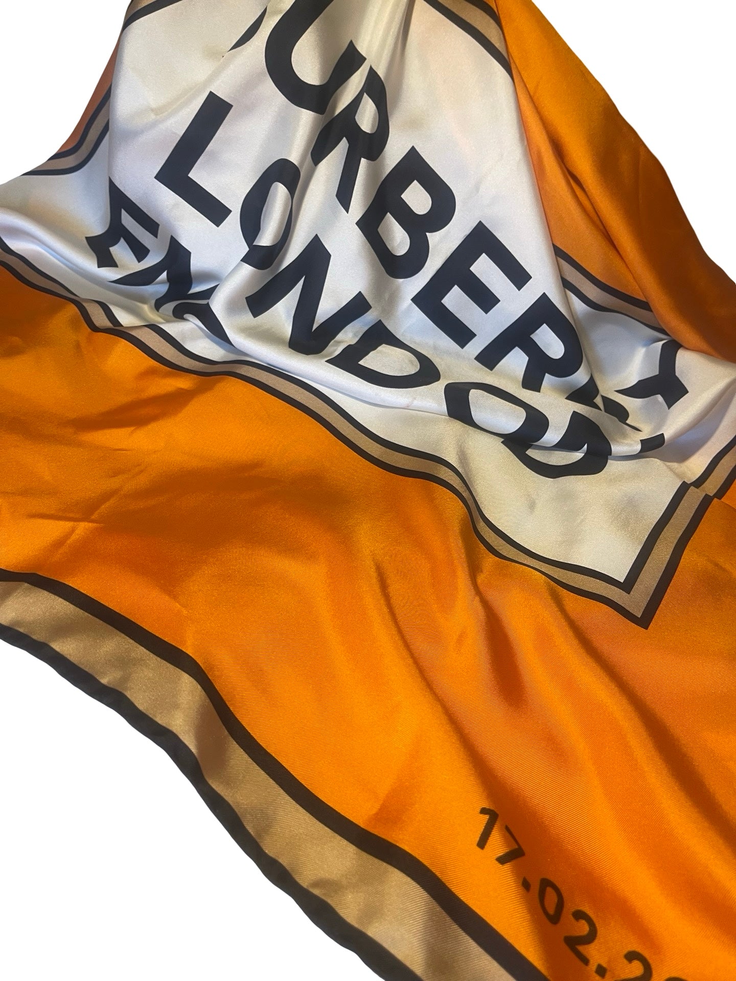 A close-up of a Burberry London silk scarf featuring the iconic orange and white check pattern with black borders and text.