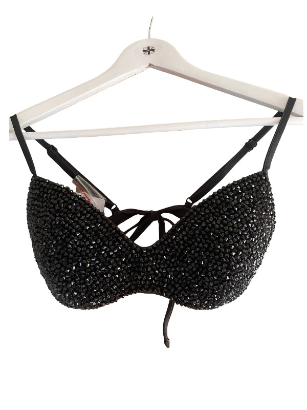 A black beaded bralette with thin straps and a front tie closure, hanging on a white wooden hanger against a plain white background.