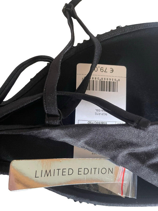 Close-up of a black bra with thin straps, showing a white price tag and a beige 'LIMITED EDITION' hangtag attached, on a white background.
