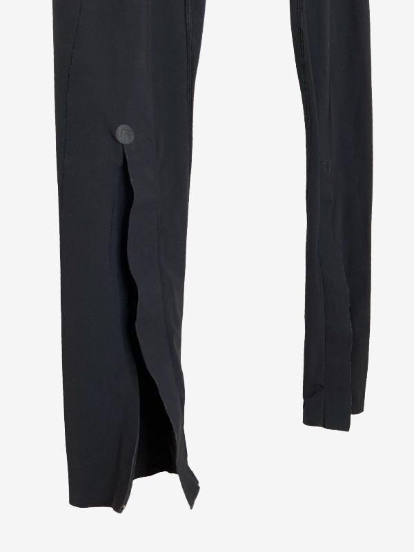 Close-up of black trousers showing a side slit with a button detail on one leg and the side seam of the other leg, against a plain white background.