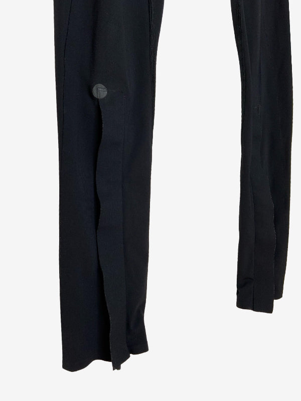 Close-up of black trousers showing a side button detail and the side slit hem on a light gray background.