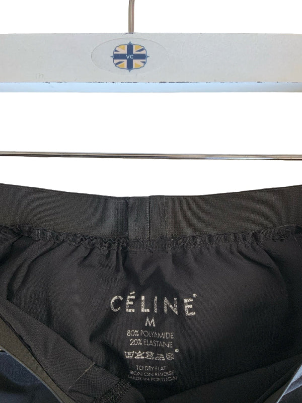 Close-up of the inside waistband of black Céline leggings on a white hanger, showing the printed brand name and size M.