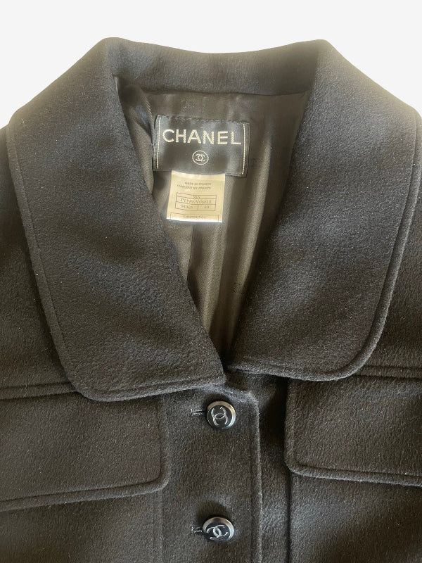 Close-up of a black Chanel jacket with a wide collar, button closure, and a visible Chanel neck label.