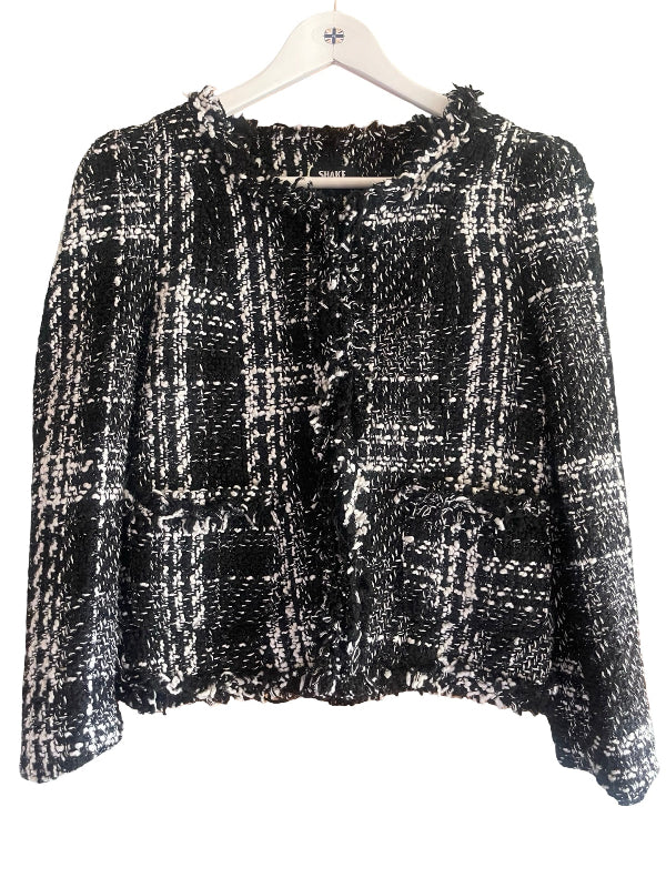 A black and white tweed plaid cropped jacket with long sleeves and a ruffled front, hanging on a white wooden hanger against a white background.