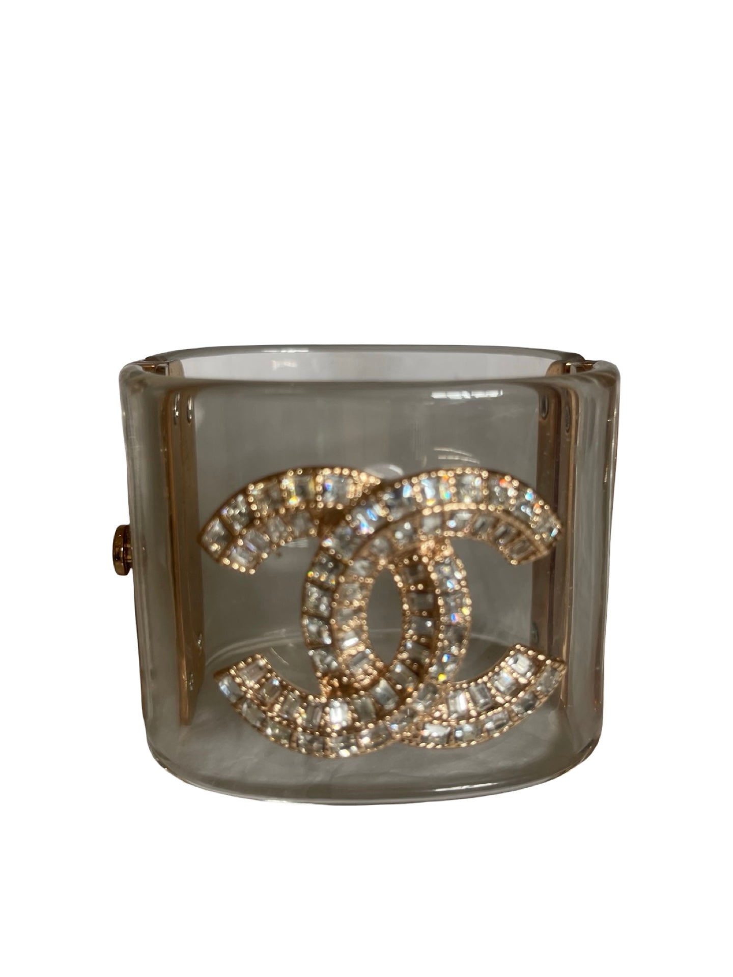 A Chanel cuff bracelet made of clear Perspex translucent with a large gold-tone interlocking CC logo paved with clear crystals, shown on a plain white background.