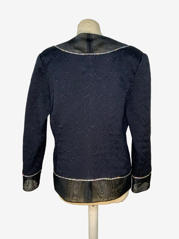A black  textured jacket with sheer black mesh trim at the collar, cuffs, and hem, displayed on a mannequin against a light gray background.