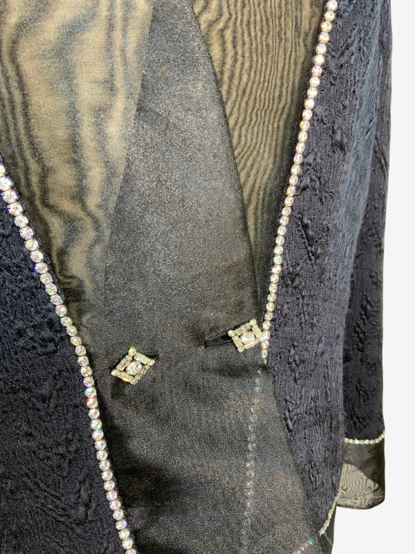 Close-up of a black textured jacket with a shimmering gold inner lining and decorative rhinestone trim along the edges.