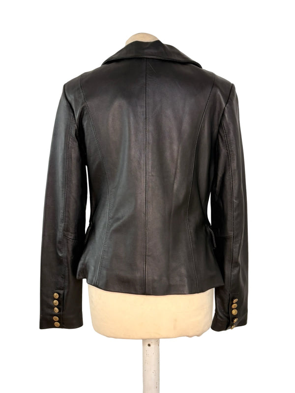 A black leather jacket shown from the back on a dress form mannequin, featuring a high collar, long sleeves with gold-tone button details at the cuffs, and a structured silhouette.