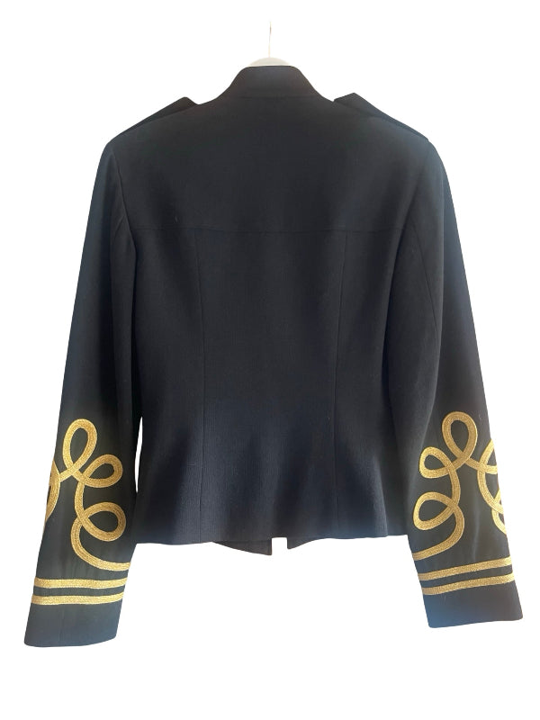 A black cropped jacket with long sleeves, featuring ornate gold embroidered scrollwork and stripes on the cuffs, shown on a white hanger against a white background.