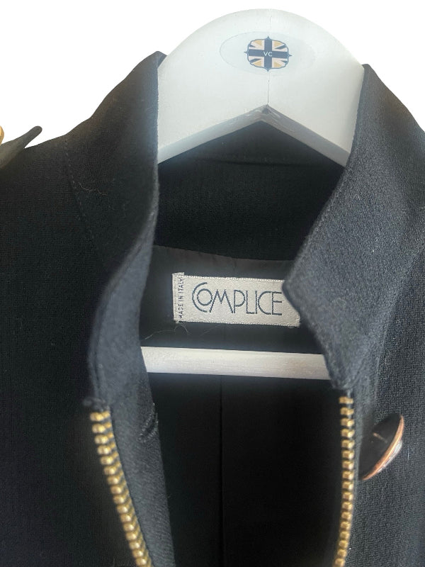 A close-up of a black wool jacket with a high collar and gold-tone zipper, hanging on a white hanger. The brand label 'Complice' is visible inside the collar.