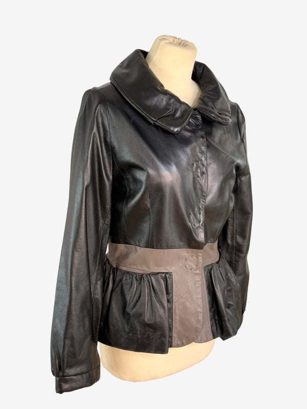 A black faux-leather jacket with a wide collar and a contrasting taupe peplum waist sash, displayed on a beige mannequin torso against a white background.