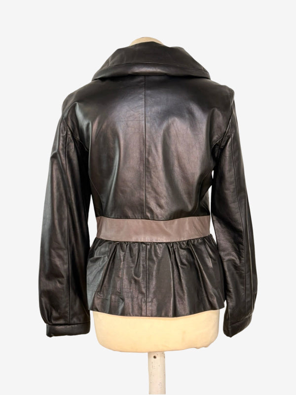 A black faux leather jacket with a wide collar and a contrasting taupe waist belt, displayed on a cream-colored mannequin torso against a white background.