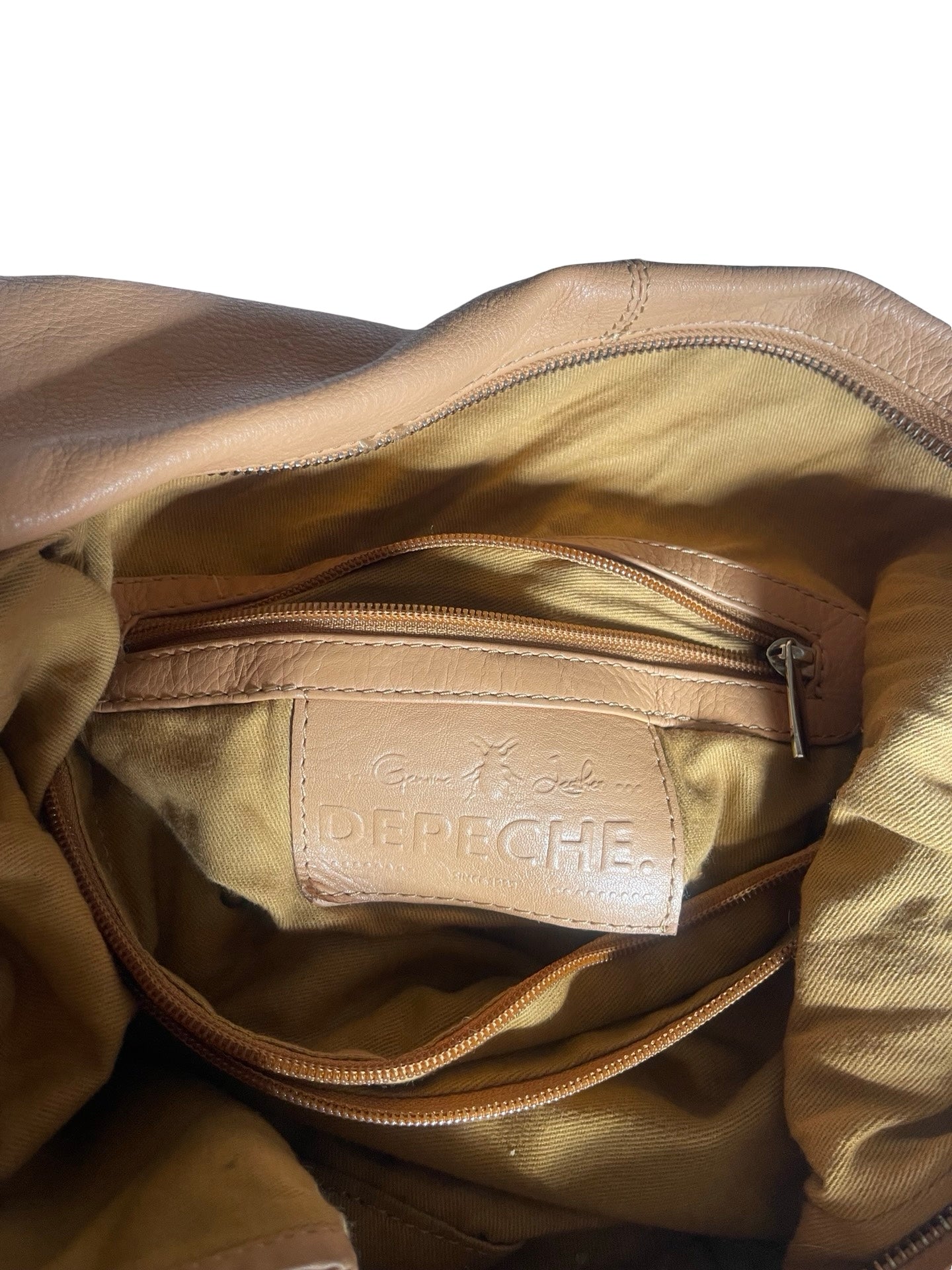 Close-up of the interior of a beige leather shoulder bag, showing a zippered pocket with a tan leather label embossed with the brand name 'DEPECHE'.