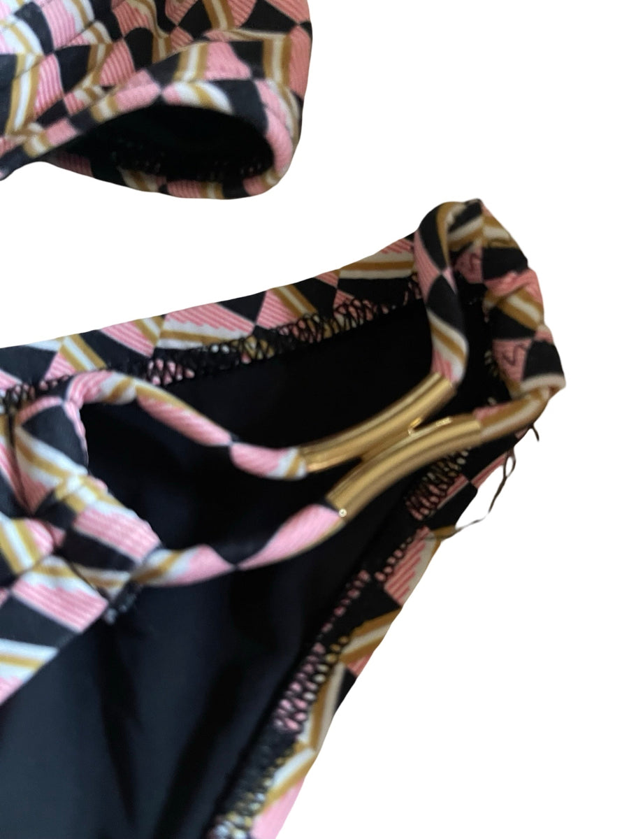 Close-up of a patterned bikini top or swimwear neckline with a geometric print in black, pink, beige, and white, featuring a black interior lining and a gold-tone metal trim