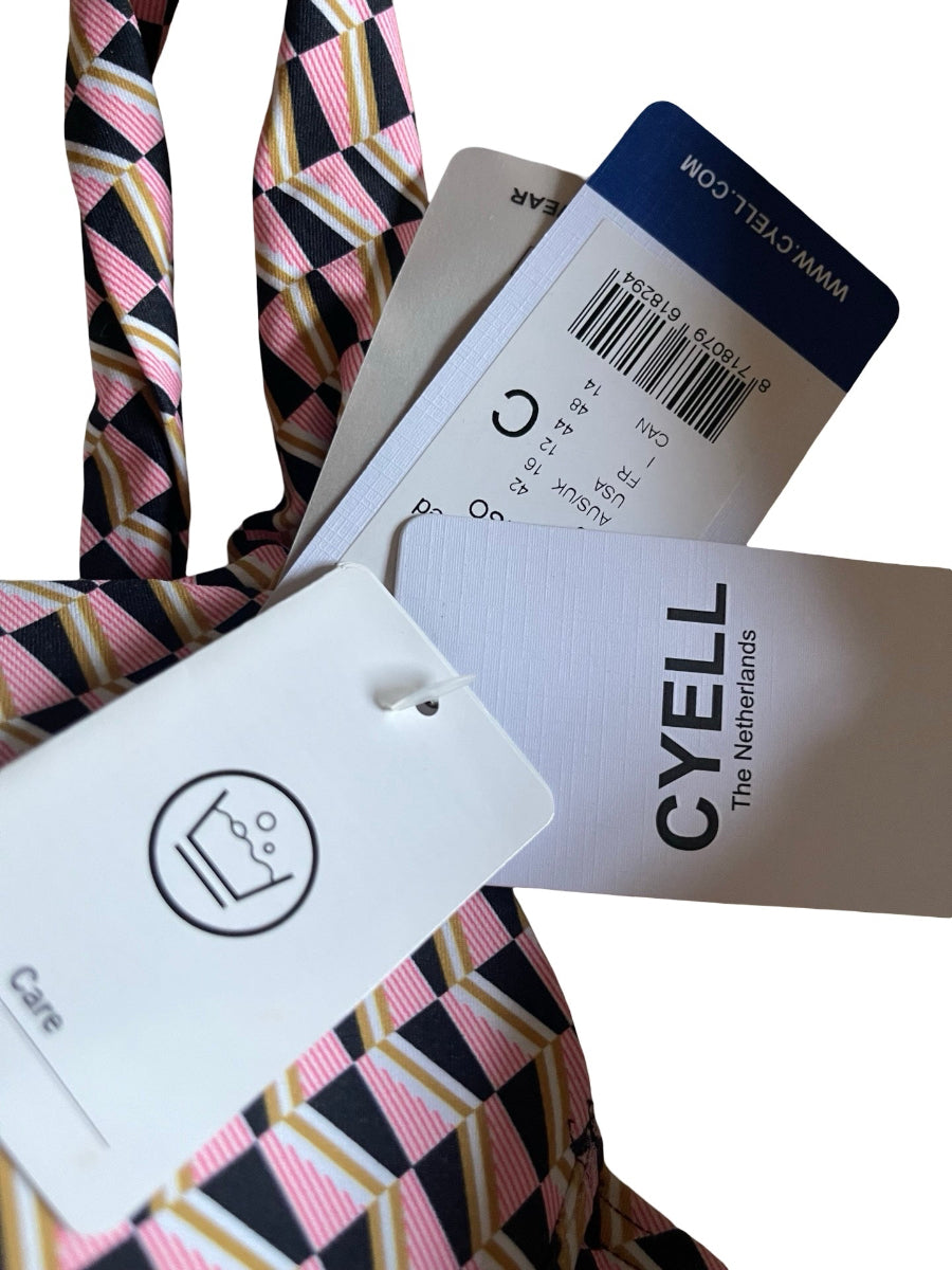 A close-up of a patterned necktie with pink, black, and beige geometric stripes, accompanied by multiple paper tags including a white Cyell care tag and a blue WWW.CYELL.COM