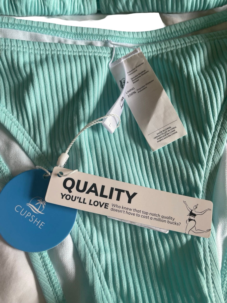 Close-up of mint green turquoise  ribbed bikini bottoms with attached white product tags, including a blue circular tag reading CUPSHE and a white tag reading QUALITY YOU'LL LOVE.