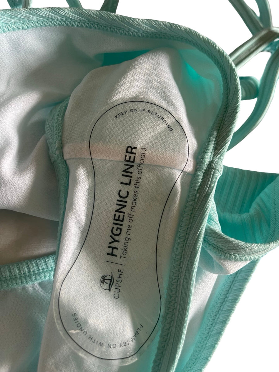 Close-up of a Cuisine Hygienic Liner underwear insert, showing the white paper liner with black printed text and branding, surrounded by mint green ribbed fabric.