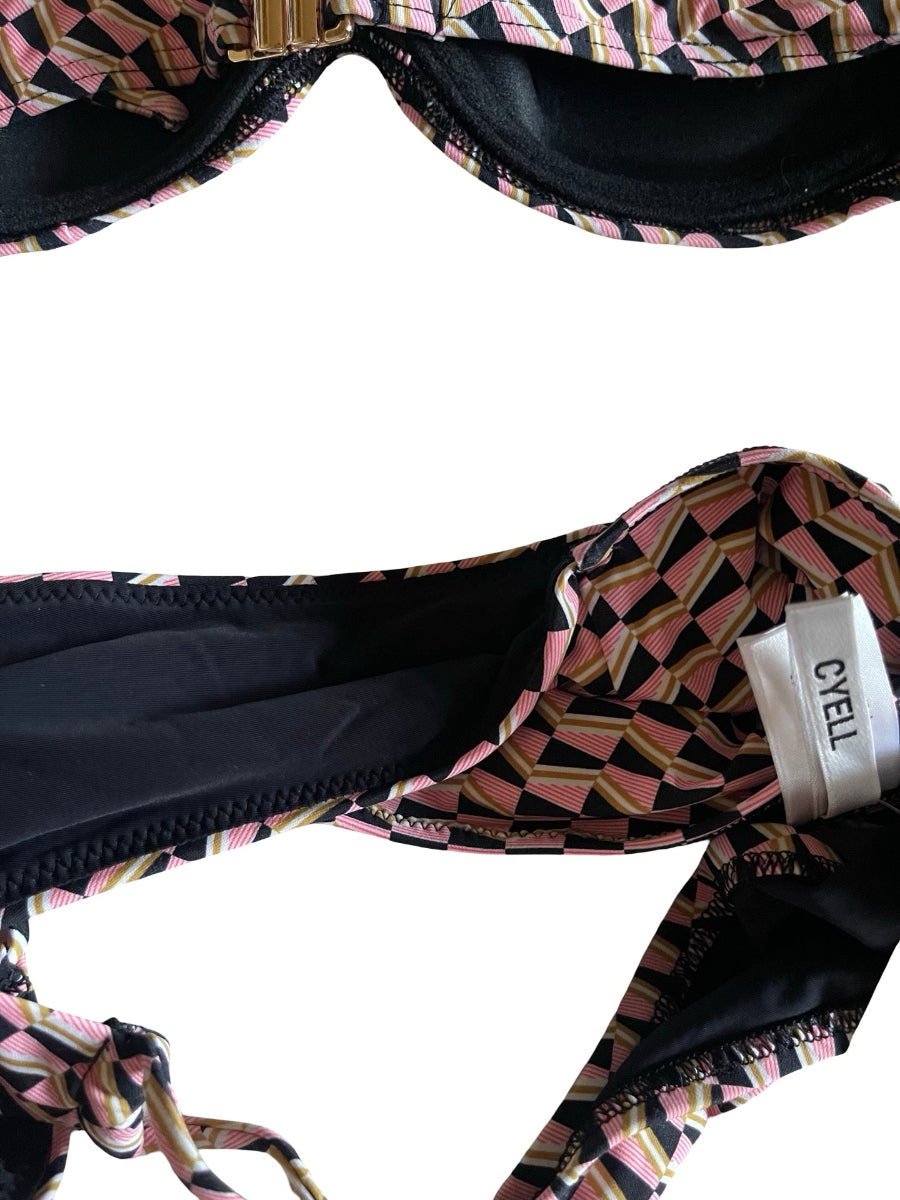 Close-up of a bikini top showing the patterned fabric, black lining, and a visible CYELL brand tag on a white background.