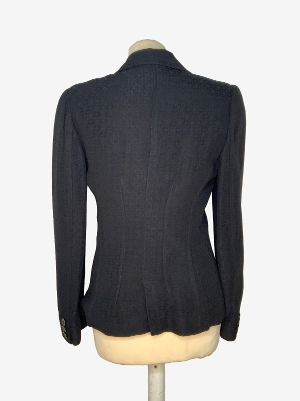 A black textured  fabric tailored blazer shown from the back on a cream-colored mannequin torso, set against a plain white background