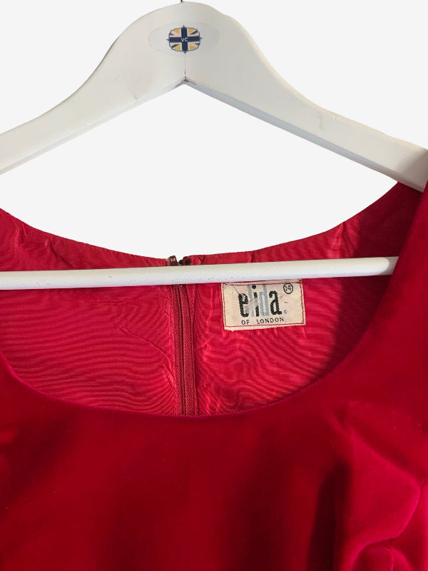 A close-up of a bright red garment hanging on a white hanger, showing the neckline, zipper, and a visible brand label reading ‘elida london’