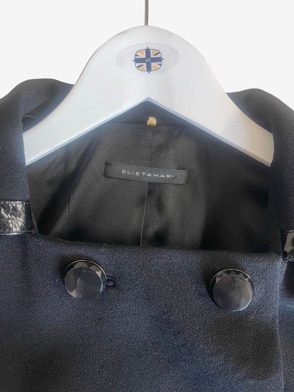 A close-up of a black wool jacket  hanging on a white hanger with a visible ELIE Tahari label inside the collar.