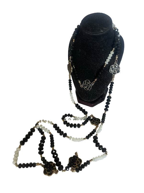 A multi-strand beaded necklace displayed on a black velvet jewelry bust against a white background. The necklace features black and white beads with bronze-toned metal charms, including a floral motif and a lotus flower.